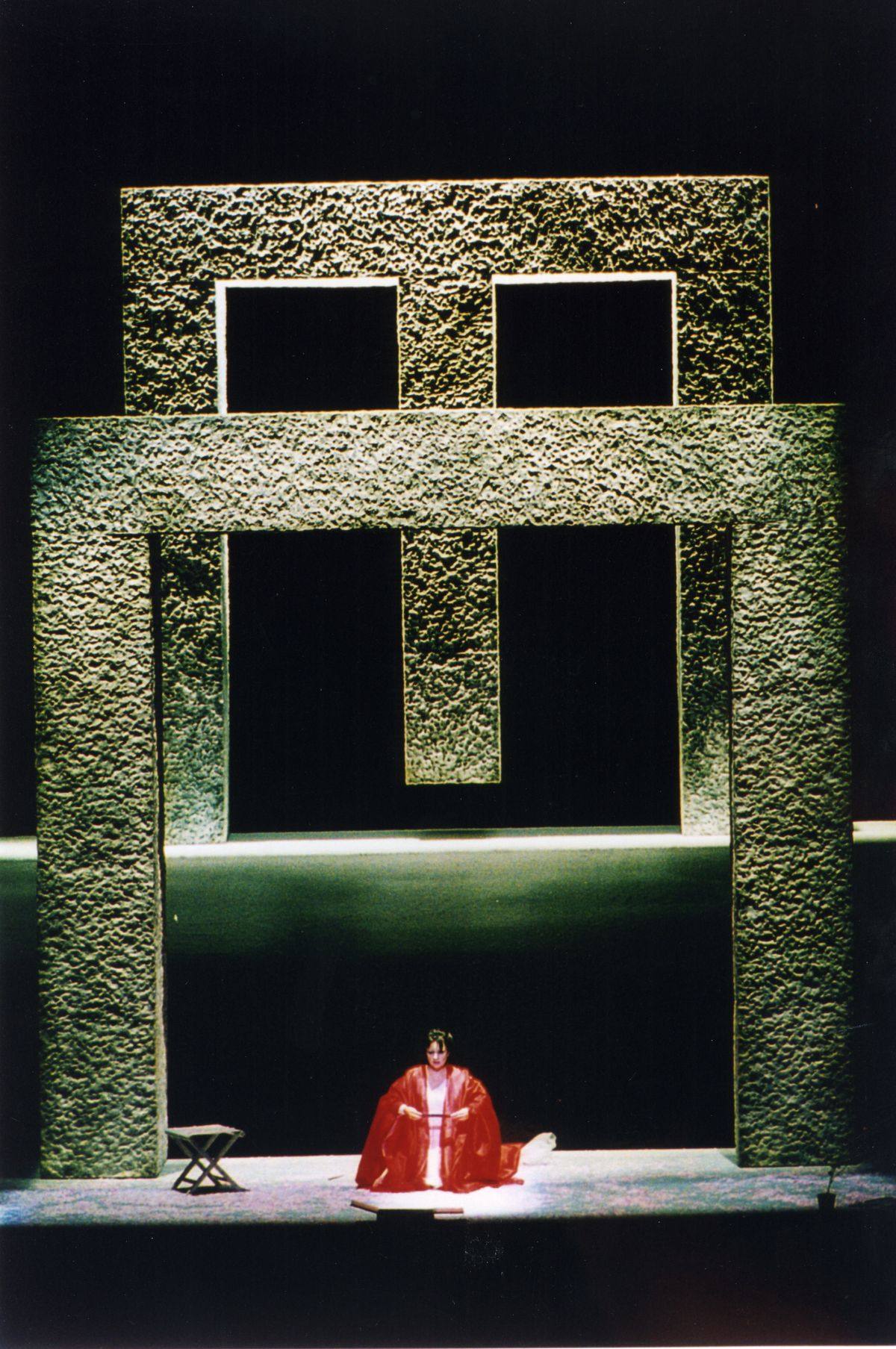 Scena di Madama Butterfly con una grande scultura in pietra a forma di portale e la protagonista in kimono rosso